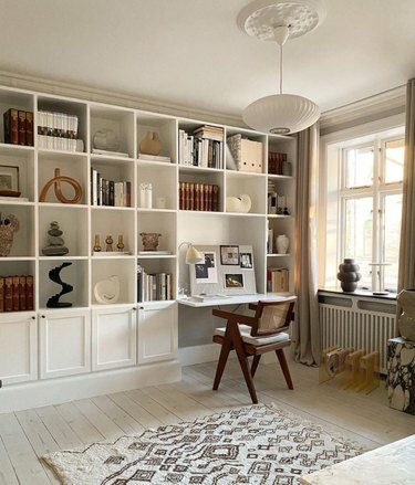 Ingebouwde boekenplanken en bureau, hanglamp, stoelen, kunst, boeken, vloerkleed.