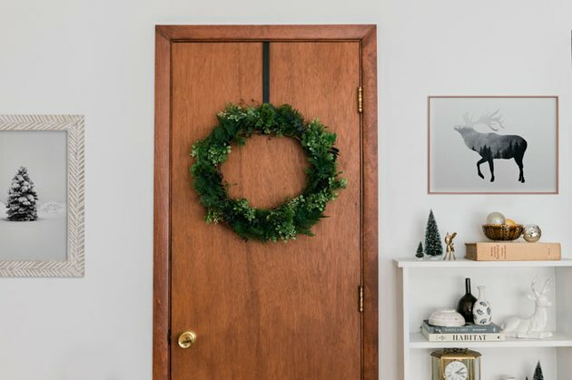 Ideia de decoração de Natal com coroa de flores falsa perene na porta de madeira com arte emoldurada e estante branca