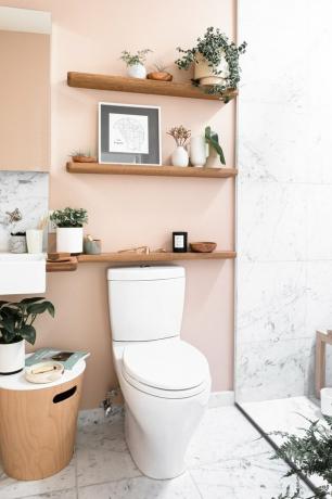 toalett med lys rosa vegg, tre trehyller og dekorasjoner