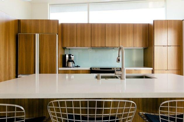 köök naturaalsest puidust kabinettidega, köögisaar valge kivi tööpinnaga ja klaasist backsplash