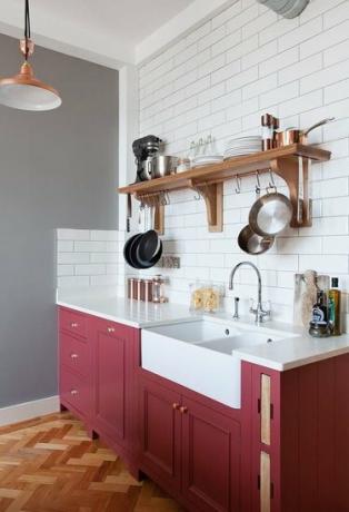 Køkken med rødbrune underskabe, hvide undergrundsfliser og grå vægge