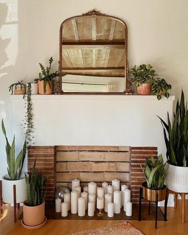 uma lareira cercada por plantas e decorada com velas cilíndricas brancas simples