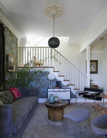 غرفة معيشة مع ورق حائط منقوش وأريكة رمادية مخملية وكراسي عتيقة