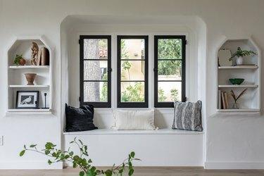 Tre finestre magre sono dipinte con rifiniture nere sopra una panca incorporata e scaffali incorporati