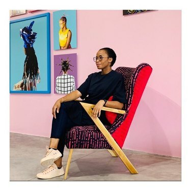 Ο σχεδιαστής επίπλων Tosin Oshinowo κάθεται σε μια πολύχρωμη καρέκλα με ξύλινα πόδια