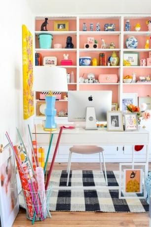 escritório em casa branco com estante pintada de rosa atrás de uma mesa de escritório branca, tapete xadrez