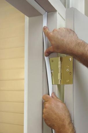 En hvid mands hænder installerer vejrbeklædning på en hvid dør