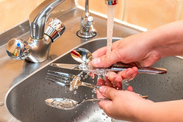 Kvindelige hænder, der vasker bestik under rindende vand i køkkenet, hænderne tæt på