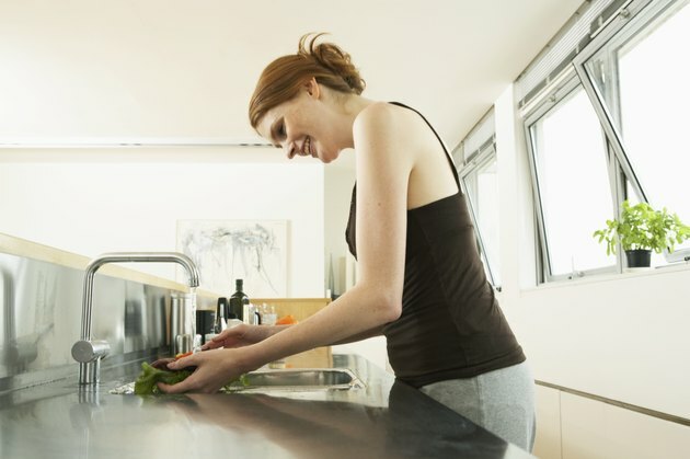 Noor naine peseb salatit köögivalamu juures, naeratab, külgvaade