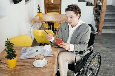 mulher em cadeira de rodas à mesa com laptop e café