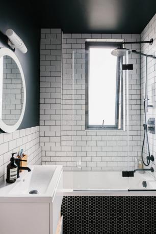 Banheiro de azulejos brancos com teto preto, chuveiro prateado, banheira e pia branca com torneira preta