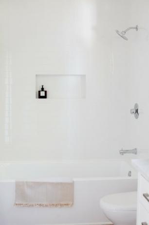 Bad med hvite vegger, hvitt badekar, hvitt toalett.