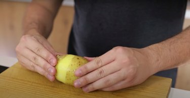 asmuo, nulupęs bulvių odą ant medienos pjaustymo lentos