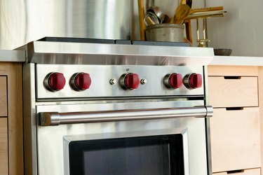 Un forno con manopole rosse. Armadietti in legno chiaro, un bancone bianco e un contenitore di utensili in legno.