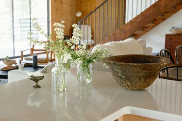 En hvit benk med blomstervaser, en trebolle og en liten tinnfat. En tretrapp i det fjerne.