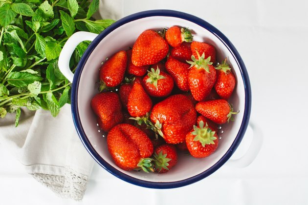 aardbeien in keramische kom naast verse groene kruiden