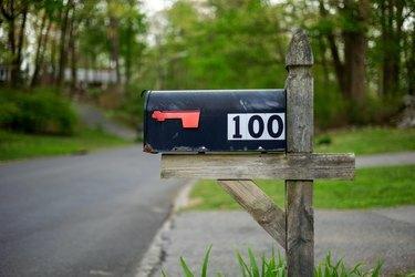 Musta postilaatikko numerolla 100 valkoisella kiinnitetty puiselle jalustalle tielle amerikan maaseudulla.