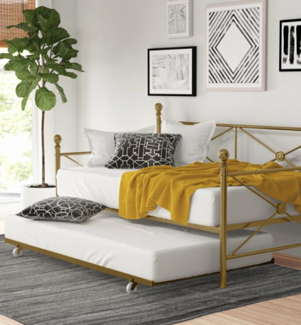 „Small Space Daybed“ idėjos su žalvarine lova su geltona antklode, pagalvėmis, augalais, daile, kilimu.
