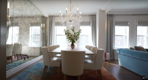 salle à manger brumeuse copeland avec lustre, chaises blanches et mur de miroir texturé