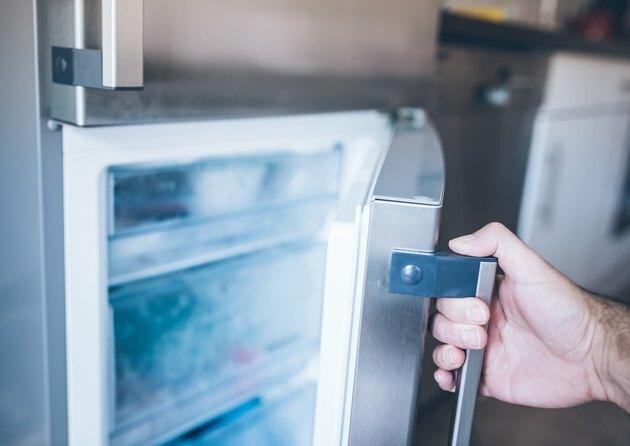 mano di un uomo che apre la porta del congelatore in cucina