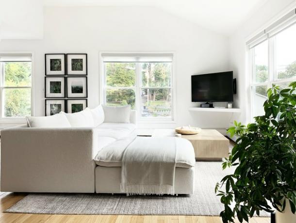 Kreminės spalvos sofa lengvai užpildytoje svetainėje