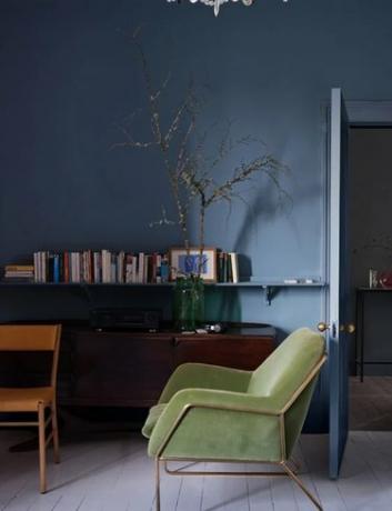 Il colore della vernice blu medio-chiaro di Farrow & Ball su una parete dell'ufficio dietro una poltrona verde e una mensola a muro ricoperta di libri.