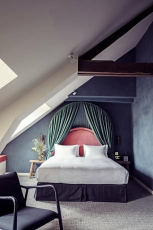 غرفة نوم بجدران أرجوانية داكنة وسرير مع لوح رأس سلمون ومظلة خضراء