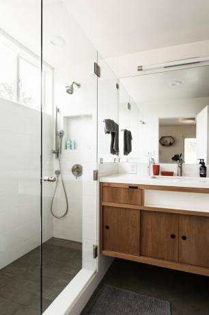 Banheiro branco com paredes de vidro do chuveiro e armários marrons