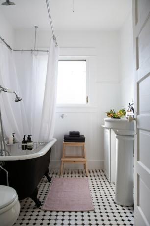 as paredes, a cortina do chuveiro e a maioria das luminárias neste banheiro são brancas; o piso é preto e branco e a banheira totalmente preta