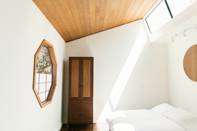 rustiek decor in kamer met licht houten panelen plafond, gewelfd plafond, dakramen, achthoek raam met ruiten en houten frame, wit beddengoed, houten kast.