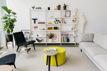 غرفة معيشة مشرقة مع طاولة قهوة صفراء ورفوف بيضاء ومقاعد
