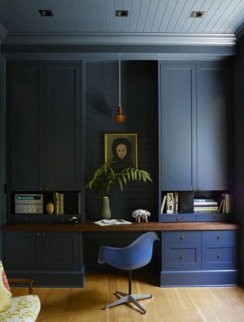 مكتب بخزانة زرقاء داكنة وكرسي ايمز وسقف خشبي باللون الأزرق