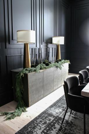 Sala de jantar preta com parede de realce preto, velas cônicas, lâmpadas de latão e enfeites verdes
