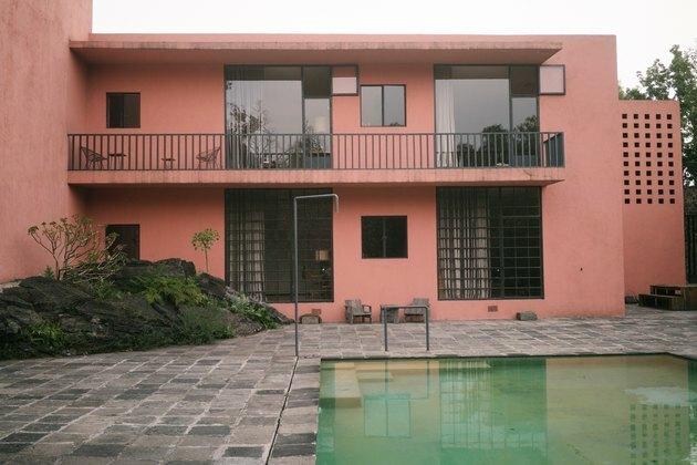 Pátio de ardósia com piscina e edifício rosa de meados do século com grandes janelas e varanda.