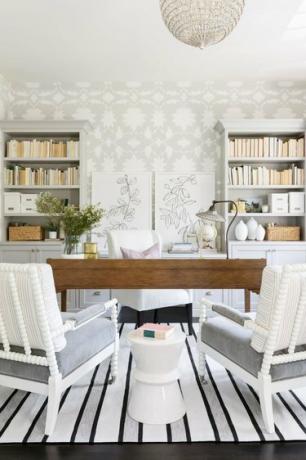 escritório doméstico cinza com papel de parede floral cinza e branco e mesa de madeira