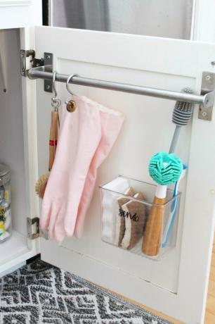armazenamento sob a pia com barra de toalha com luvas rosa e escovas penduradas na porta do armário branco