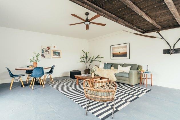 Sala de estar em um apartamento contemporâneo de estilo boêmio da Califórnia: piso de cimento, teto de madeira, ventilador de teto, tapete preto e branco, cadeira de vime, planta, mesa de centro e sofá