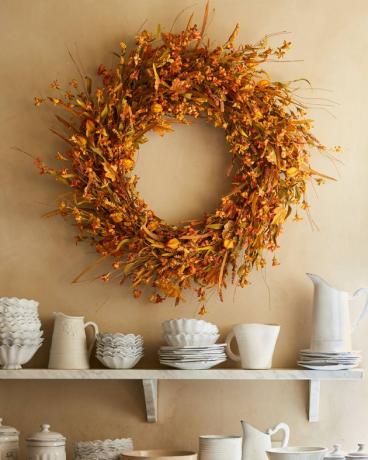 herfstkrans gemaakt met forsythia die boven een plank met borden hangt