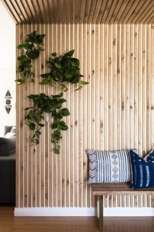 En vegg av trepanel og hengende planter og en trebenk med Shibori-puter.