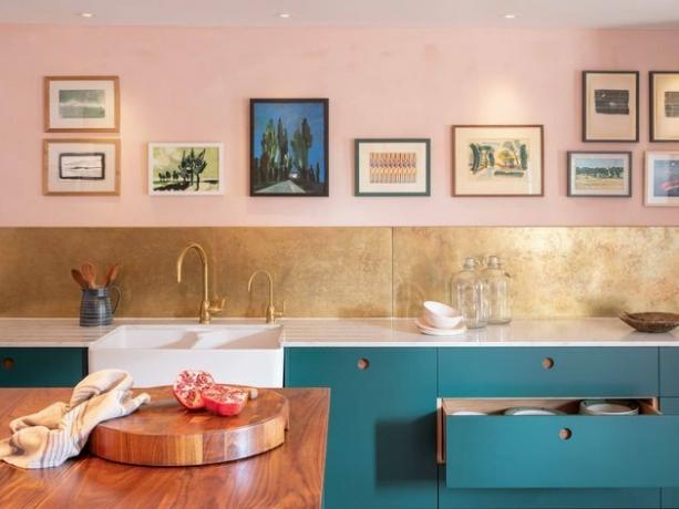 roze kamerideeën met roze muren, gouden backsplash, groenblauwe kasten, houten aanrecht, koperen gootsteenkraan in de keuken.