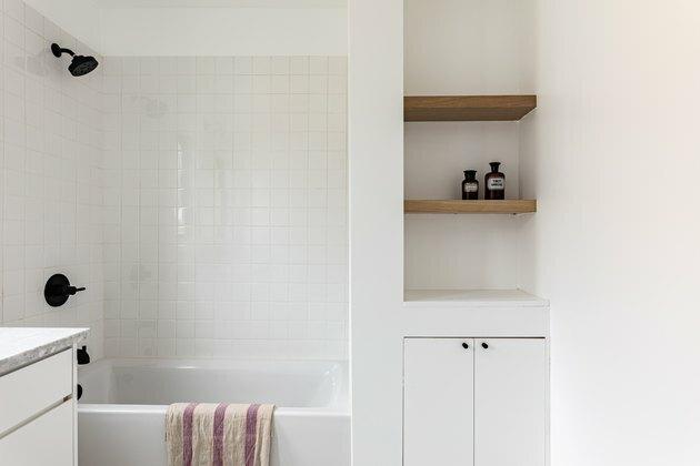 ladrilho branco, banheira e chuveiro combinados em branco, prateleiras embutidas em madeira