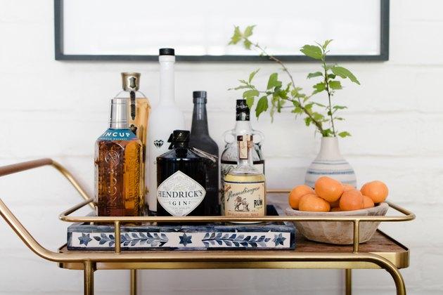 Carrinho de Bar Latão Contemporâneo com garrafas de licor, cesto de laranjas.