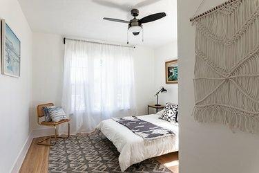 Een slaapkamer met een macramé hangend en transparante gordijnen opgehangen