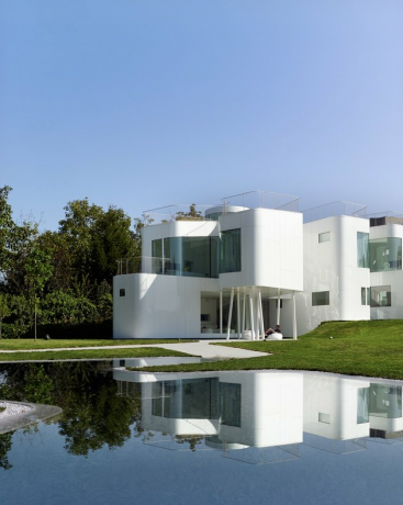 Residência em estilo Bauhaus com exterior branco e grandes janelas ao lado do lago