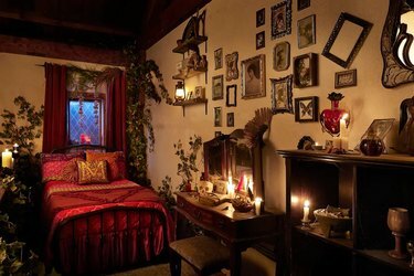 Il loft di Mary Sanderson nell'Hocus Pocus Cottage con un letto rosso, una scrivania di legno con candele e cornici storte che coprivano il muro.