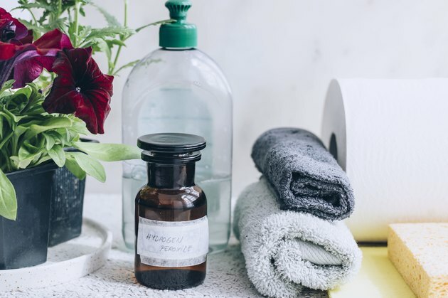 kleine bruine fles met het label waterstofperoxide naast twee kleine handdoeken, papieren handdoek, zeepfles en plant