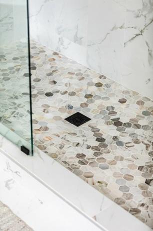 Um chuveiro com portas de vidro e piso frio neutro cinza-branco
