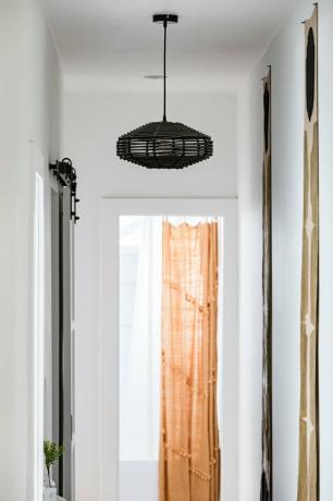 Ideias para iluminação de corredor com uma luz suspensa abstrata preta em um corredor de parede branca e uma cortina laranja