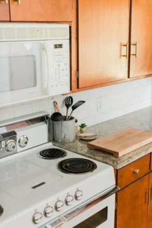 Ξύλινα ντουλάπια κουζίνας, πάγκοι από γρανίτη και πλακάκια από λευκό πλακάκι με φούρνο μικροκυμάτων και εστίες μαγειρέματος