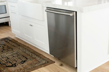 Rustfri opvaskemaskine i hvid køkkenø. Marmorbordpladen strækker sig over opvaskemaskinen. På gulvet et lille tæppe.